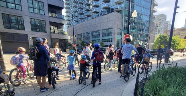 A large group of riders stopped at a crossing beneath the River North towers